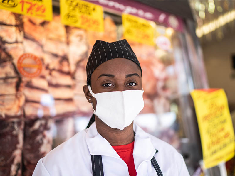 Portrait of female butcher working at butcher's shop - with face mask