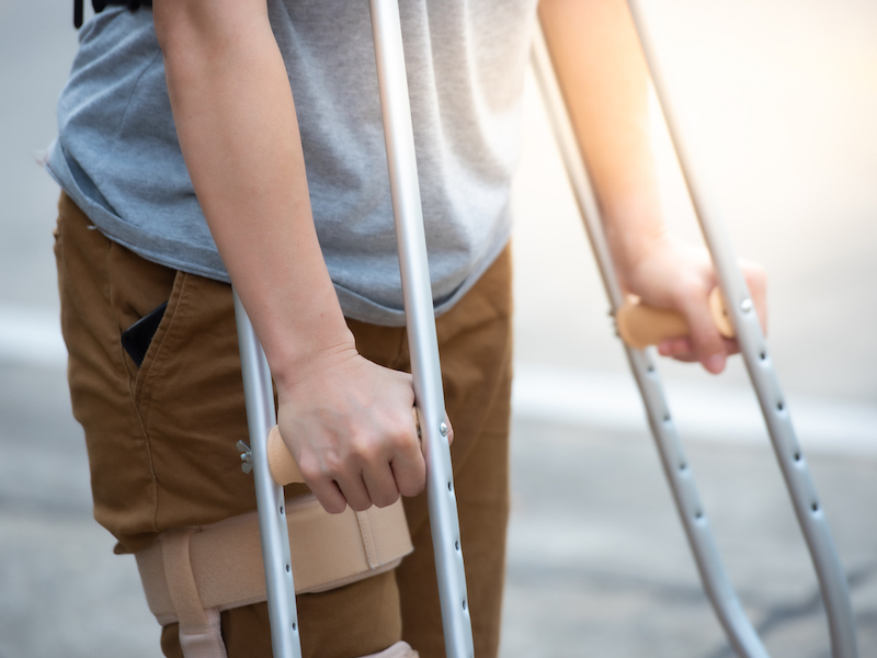 Disabled woman with crutches or walking stick or knee support standing in back side,half body.