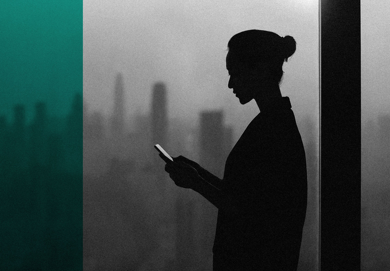 Silhouette of young woman using smartphone next to window with cityscape