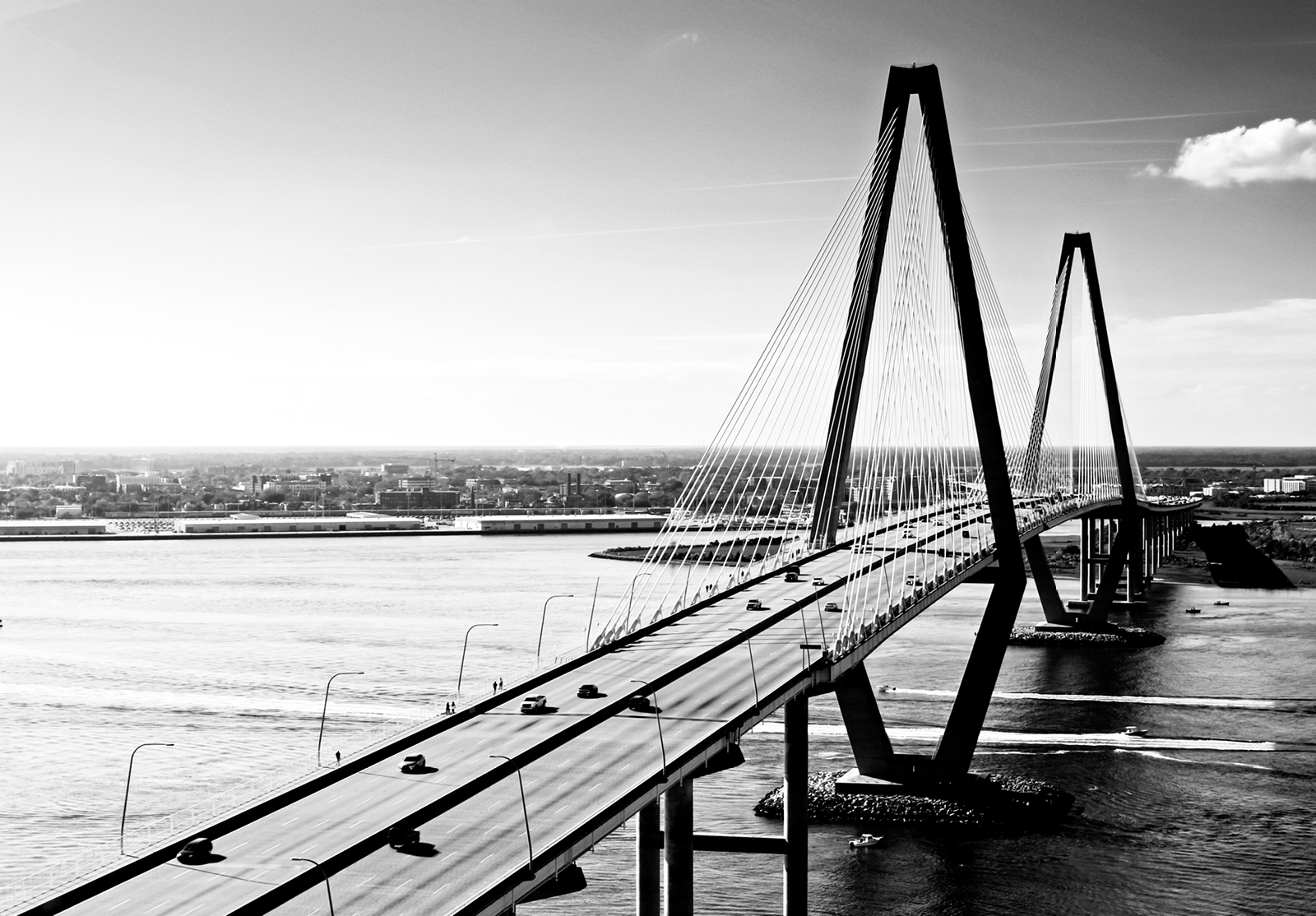 Black and white photo, large bridge with cars on it, over water.