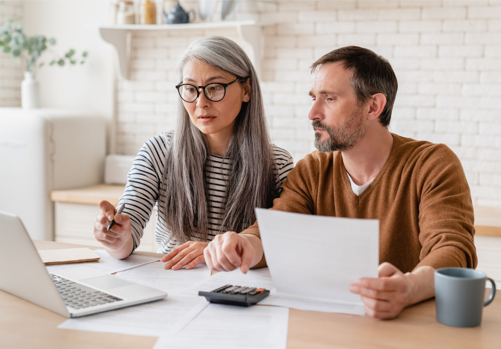 Mature middle-aged couple sitting in front of laptop and calculator, calculating finances