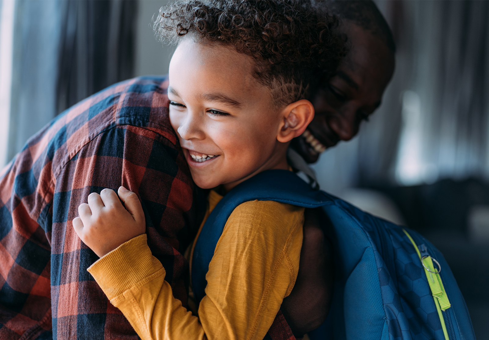 Adult and small child with backpack, hugging and smiling