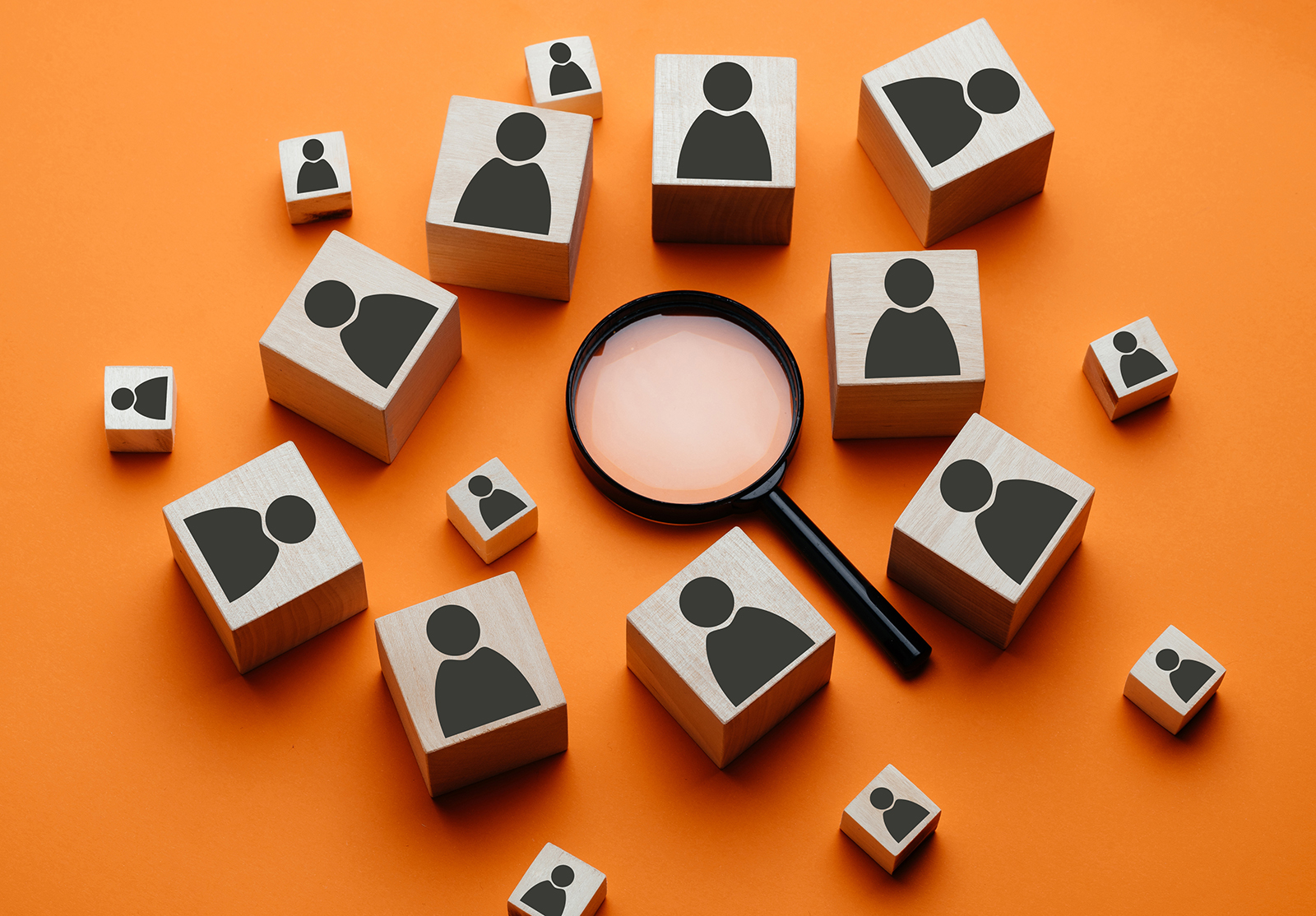 Wooden cubes with the image of a man lie next to a magnifying glass on an orange background. The concept of talent search or employee concept search using a magnifying glass.