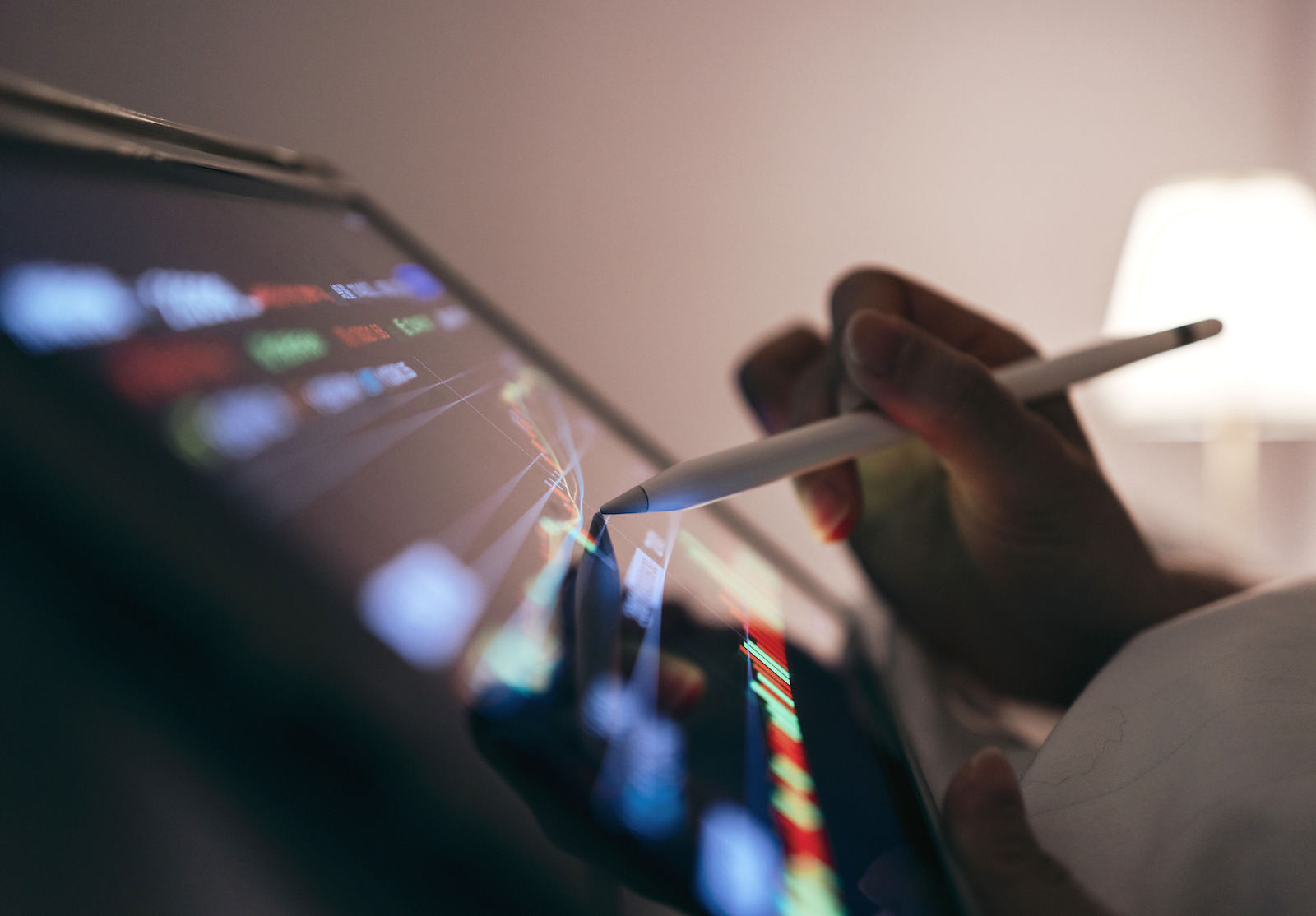 Close-up of a woman using a tablet in bed tracking the technical movement of a stock chart on a computer screen. alternate text for this image