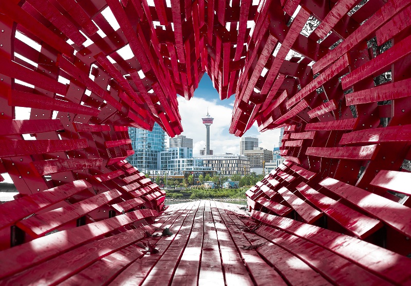 The Calgary skyline, including the Calgary Tower, framed by a large red wooden sculpture shaped like the Candian flag.
