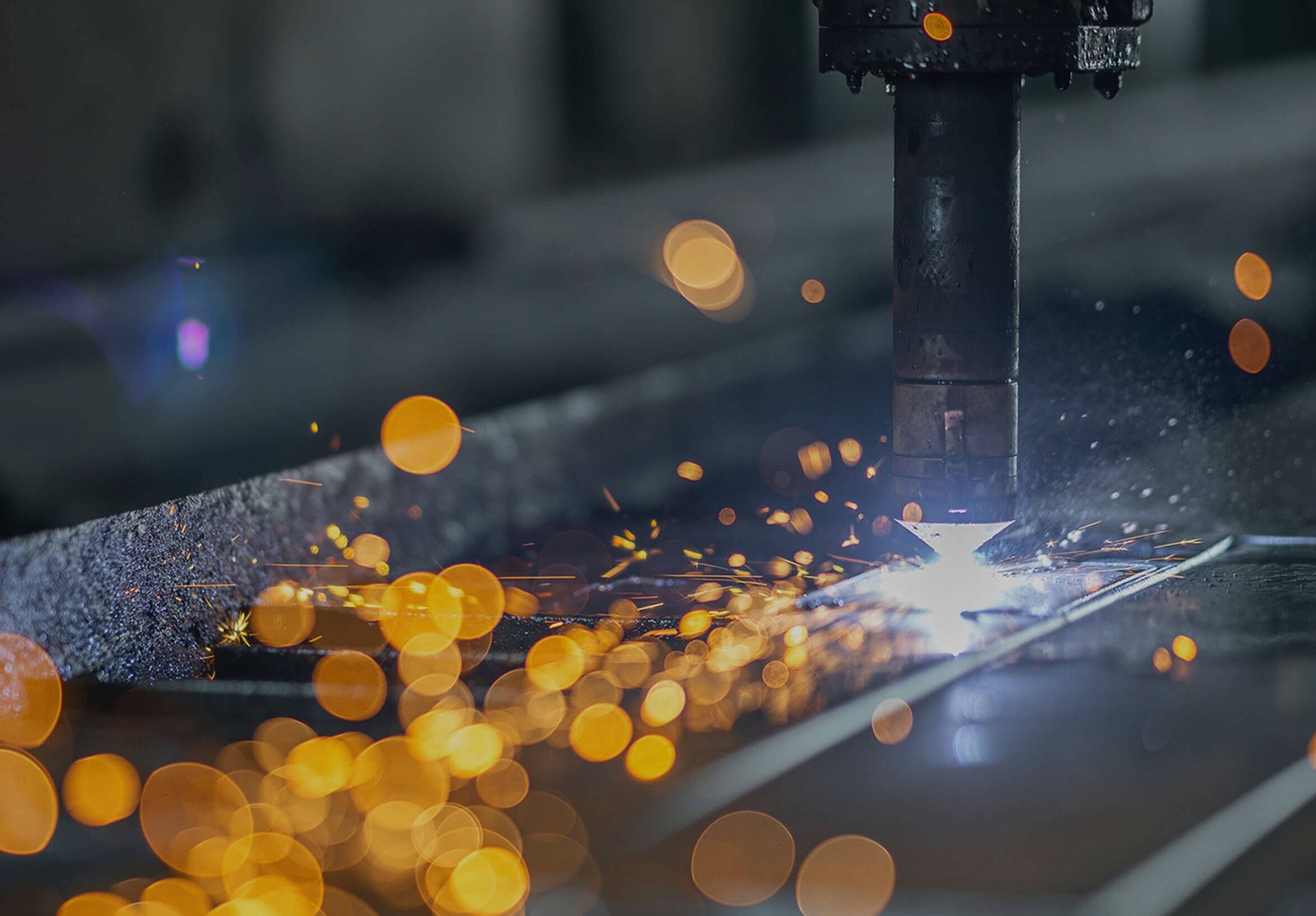 Plasma cutter slicing through metal, emitting bright sparks and intense light in a dark industrial setting.