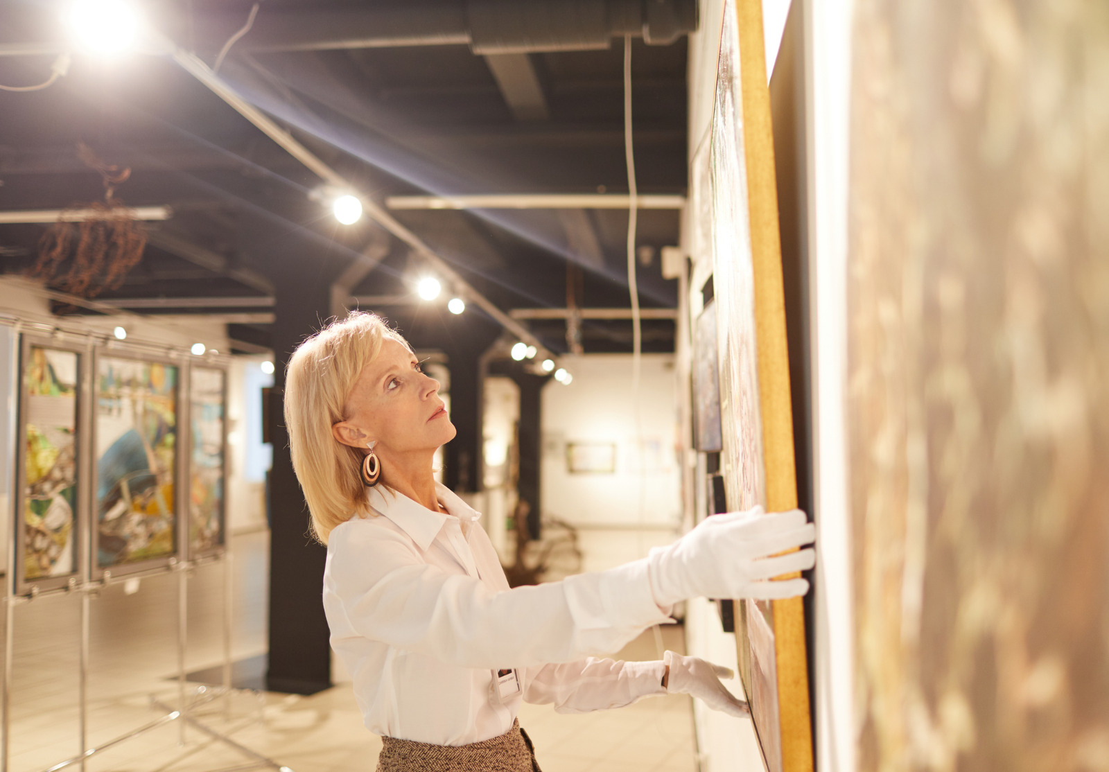 Mature Woman Hanging Paintings in Art Gallery