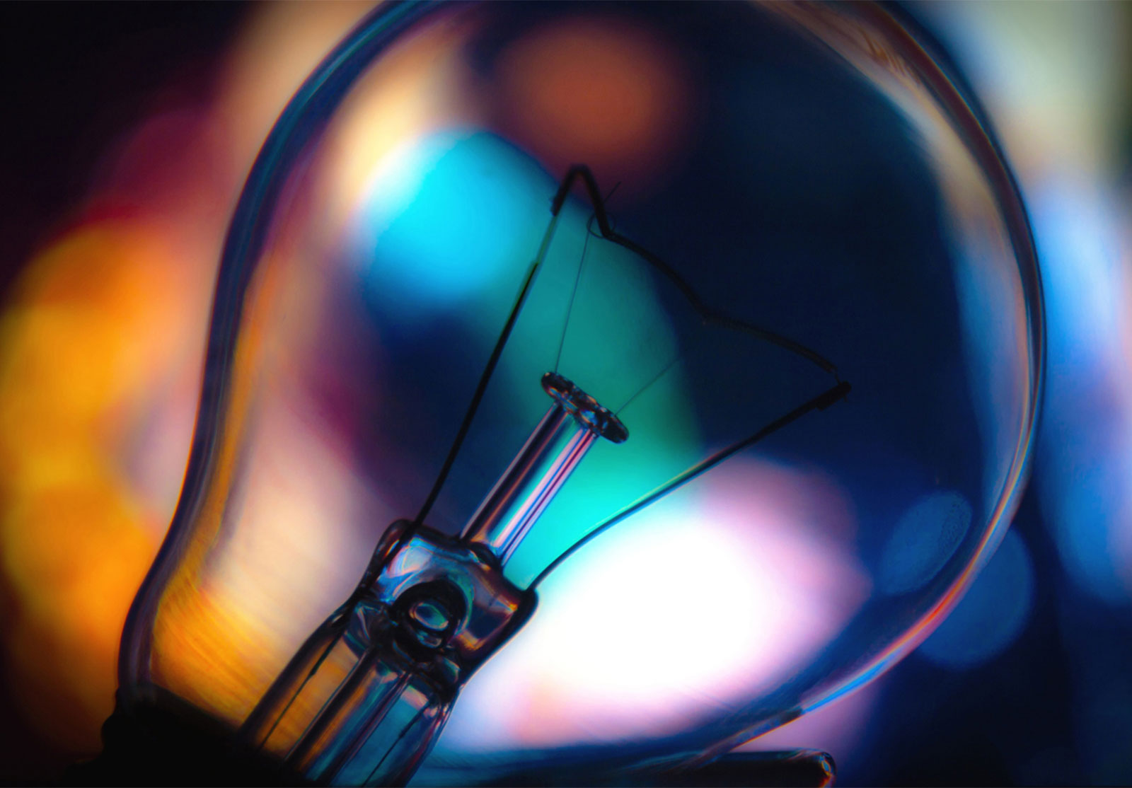 Close-up of a light bulb filament with colorful, out-of-focus lights in the background.